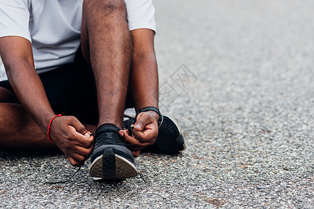 坐在鞋带上尝试跑鞋的黑人男子运动员活动衬衫慢跑者跑步运动鞋健身房黑色男性体育场图片