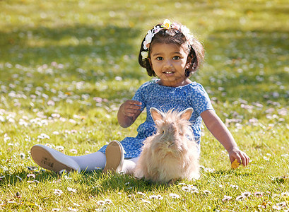 一个小亚洲女孩 和家里的兔子坐在绿色草地上图片