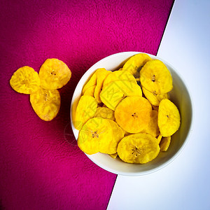 香蕉薯片保存在碗中 粉红色背景的美容小吃营养热带黄色筹码桌子勺子甜点早餐香蕉图片