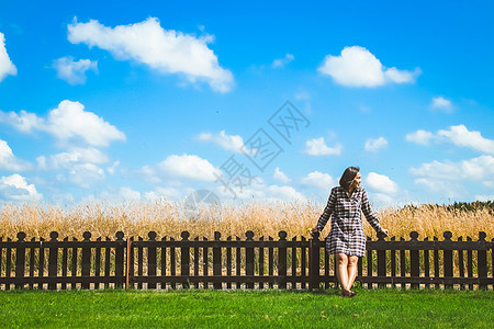 快乐的少女站在青云天空下的绿地上与木栅栏并肩站在一起女士晴天蓝色土地国家场地地平线太阳木头草地图片