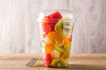 木制桌上塑料杯中的新鲜切水果塑料红色食物奇异果橙子杯子西瓜黄色绿色图片