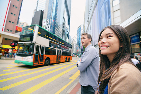 香港人步行等待交通灯光和双层甲板巴士通过繁忙的公路 你们这些亚裔中国人/高加索男女在城市中快乐地生活在一起 微笑着笑容图片
