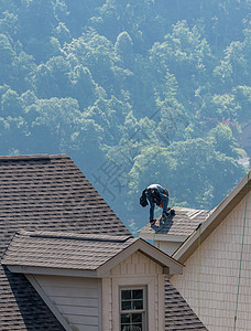 年轻房顶承包商在地面高处的屋顶上钉钉吊坠卵石安装男人建筑工人屋顶木匠瓦片体力劳动者建设者瓷砖图片