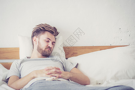 英俊的年轻美国男子在家中床上睡觉     保健车枕头酒店男人卧室成人休息说谎睡眠男性闲暇图片