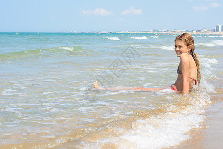 一个十岁的女孩坐在水中 在一个空海岸上图片