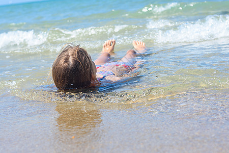 一个女孩躺在她背上 浅水在海沙海岸图片