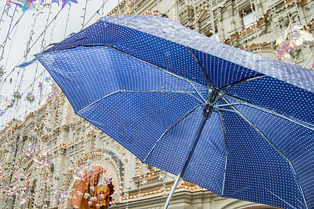 在城市街道背景的露天大雨中 用小波尔卡点特写了一只有小波尔卡圆点的开放蓝伞图片