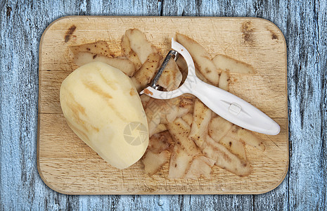 Raw马铃薯在木制砍板上剥皮 并用削皮机在一个泡球上剥皮图片