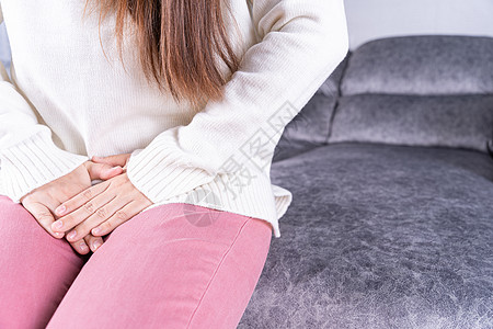 妇女在家中坐在沙发上时 手握着她的膝盖 肚子疼 吃不饱 在医疗或日常生活概念方面女孩疾病腹胀伤害疼痛便秘女士身体经期腹痛图片