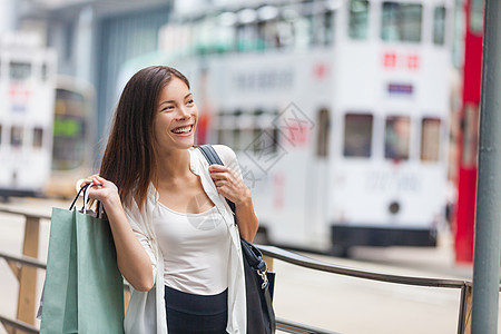 亚洲女性下班后提着购物袋走在城市街道上 花钱在香港市中心买时装 城市生活年轻人的生活方式 快乐的多种族女孩图片