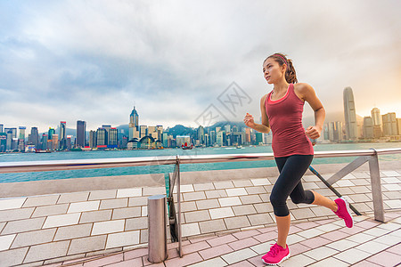 城市跑步-女子跑步者和香港天际线 女运动员健身运动员慢跑训练在九龙尖沙咀海滨长廊和星光大道上过着健康的生活方式图片