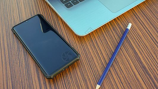 用黑智能手机和蓝铅笔 写在木制桌上的电脑笔记本日记桌子木头技术记事本工作办公室笔记键盘电话图片