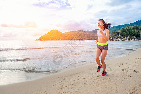 跑车的女人在日出时在海滩上奔跑工具速度运动员海洋耳机齿轮运动跑步赤脚慢跑者图片