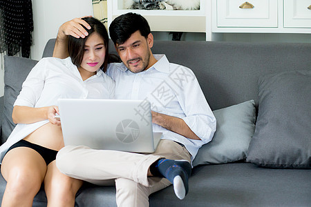 一对年轻的亚裔夫妇的肖像 夫妻坐在一起电脑女性技术笔记本腹部房子沙发女士妻子母性图片