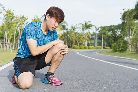 亚洲男子在跑着罗阿时用手握住膝盖受伤扭伤训练疼痛运动男性运动员肌肉痛苦赛跑者跑步图片