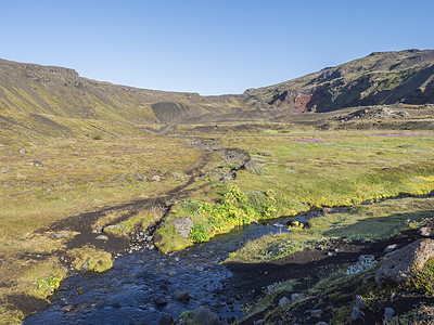 冰岛风景与蓝色河流和郁郁葱葱的绿色植被在冰岛的远足径 火山景观中的绿色山谷在熔岩场和山脉之间 清晨 夏日的蓝天溪流远足小屋营地帐图片