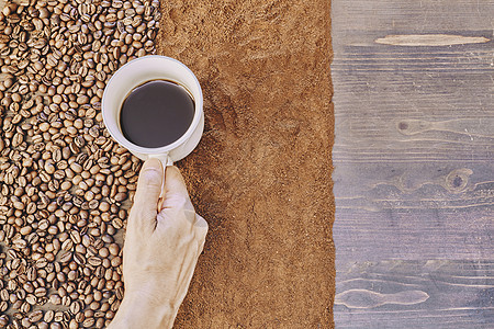 一个人在桌子上拿着一杯咖啡加烤咖啡豆和地面咖啡豆的顶层风景黑色种子木头咖啡店杯子饮料豆子棕色早餐香气图片