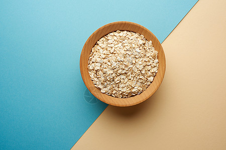 蓝色背景的棕色木碗中的粗燕麦片绿色谷物食物种子营养粮食早餐稀饭木头饮食图片