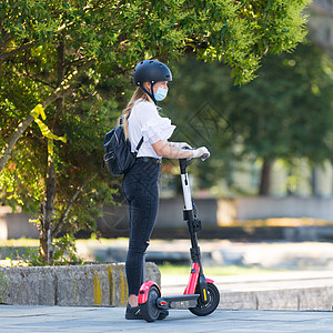 在城市环境中使用出租电动滑板车时 时髦时髦的少女在公共场合戴着电晕病毒防护面罩 斯洛文尼亚卢布尔雅那的新型环保城市交通图片