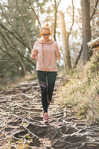 积极运动的女人在秋天的秋天森林里跑步时听着音乐 女赛跑者户外训练 户外慢跑的年轻白人女性的健康生活方式形象耳机运动装公园活动国家图片