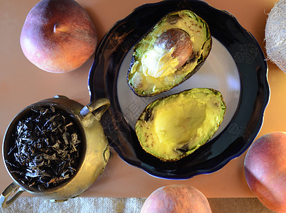盘子里有两半鳄梨 三个成熟的桃子和一小铜壶全叶茶和一个椰子图片