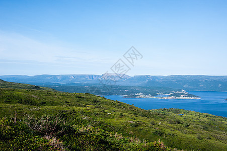 与苍蓝天空下高原相对的水面附近绿色山丘背景图片