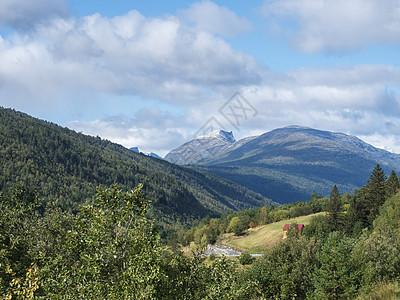 E136号公路上的隆斯达伦山谷的风景 山峰 绿林和小红黄屋有雪顶 蓝天白云背景图片