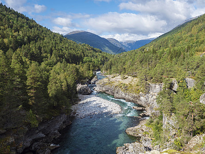 在 Romsdalen 山谷欣赏蔚蓝的 Rauma 河峡谷 山峰 岩石和绿色森林被白雪覆盖 蓝天白云背景 挪威夏季风景风光天蓝色图片