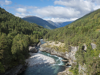 在 Romsdalen 山谷欣赏蔚蓝的 Rauma 河峡谷 山峰 岩石和绿色森林被白雪覆盖 蓝天白云背景 挪威夏季风景风光冒险旅图片