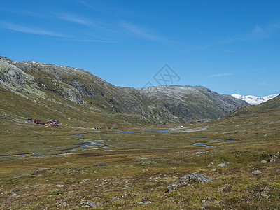 在挪威西部Jotunheimen国家公园中 红Krossbu旅游站山棚楼从高山到蓝色溪流 积雪山脉和橙色苔和热液的冰川建筑物大杂图片