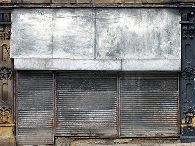 在街上一家废弃商店的前面 店前和门上有闭着肮脏 生锈的金属百叶窗零售财产窗户失败经济商业快门破产碰撞锁定图片