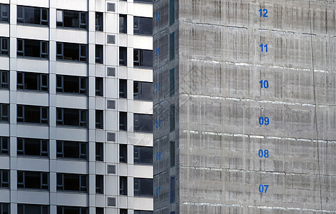 正在建设中的一栋高层公寓楼的混凝土核心筒 楼层编号用蓝色油漆标记 背景中的高塔上有银色包层房地产灰色商业服务故事数字住房进步城市图片