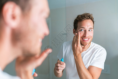微笑的年轻人在眼睛下涂面霜以治疗皱纹或眼袋 抗衰老面部护理 男性美容图片