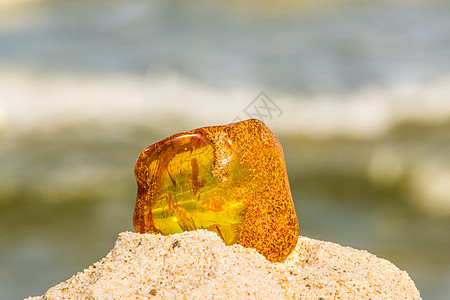 在波罗的海海滩的琥珀 和冲浪在背景中石头橙子矿物化石康复宝石挖掘海洋海滩材料背景图片