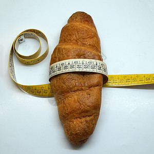 围绕羊角面包的软测量标尺 作为不健康营养的象征肥胖软尺减肥脆皮面粉甜点腰部食物小吃厘米背景图片