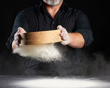 一个穿黑色制服的厨师 拿着一个圆木筛子小麦面包面团美食烘烤男性粉末灰尘厨房男人图片