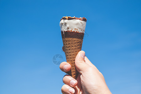 手握着蓝色天空背景的冰淇淋锥牛奶香草服务食物味道灯光巧克力奶油锥体甜点图片