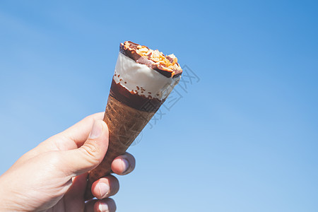 手握着蓝色天空背景的冰淇淋锥锥体香草味道巧克力灯光奶油牛奶食物甜点服务图片