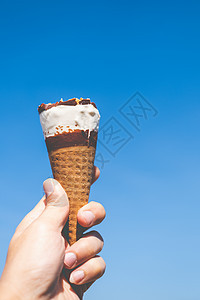 手握着蓝色天空背景的冰淇淋锥味道牛奶食物锥体灯光巧克力甜点奶油香草服务图片