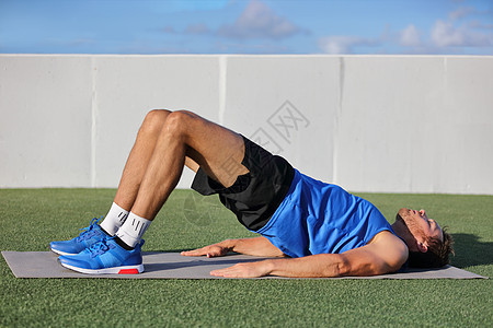 健身男子做体重臀部地板桥式瑜伽练习 适合运动员在草地上的夏季户外健身指导课上锻炼臀部肌肉和臀部图片