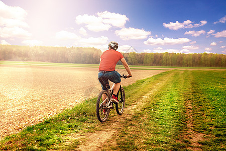骑自行车 骑自行车 在公园里 在后面的树林里有草头盔蓝色活动运动成人天空爬坡速度日落下坡图片