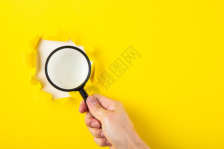 人手握着放大镜 穿过破裂的洞口侦探创造力报告检查镜片工具黄色商业背景调查图片