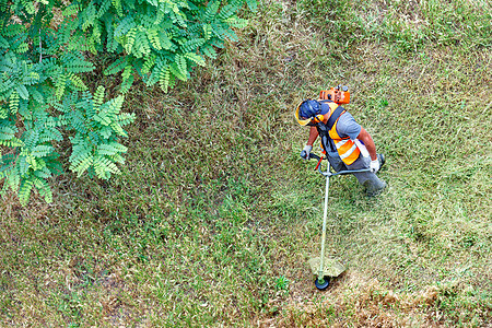 身穿防护服的工人在阿卡西亚树附近的高草上割草 顶尖视野是工业汽油短片图片