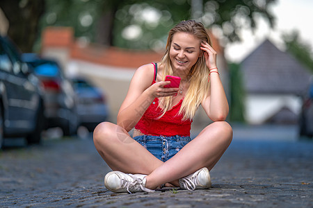 一位美丽的年轻女士的肖像 她坐在街上人行道上使用智能手机图片