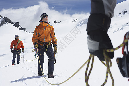 三个徒步旅行者与安全线并列 在雪山的中段背景图片
