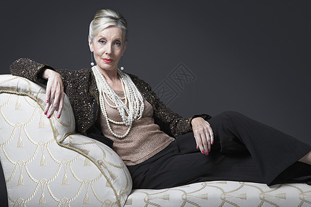在Chaise休息厅的富贵高龄妇女财富黑色珍珠时间发型魅力成人夹克影棚座椅图片