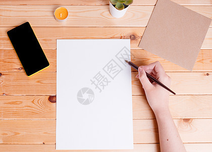 手拿着空白的白纸纸纸和一支书写笔 电话 植物圈套和一个小蜡烛放在木桌上图片
