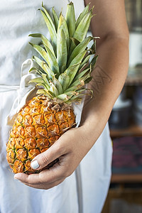 身着白色烹饪围裙的年轻女性 手里拿着一个成熟和多汁的菠萝异国衬衫男人工作营养凤梨热带蓝色躯干健康图片