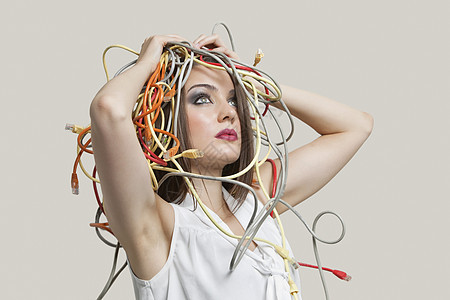 年轻女性头部缠在灰色背景的多彩电缆中图片