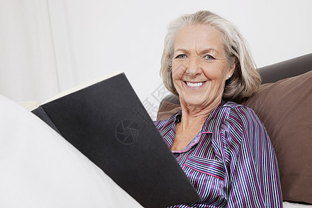 快乐的年长女人的肖像 书坐在家里图片